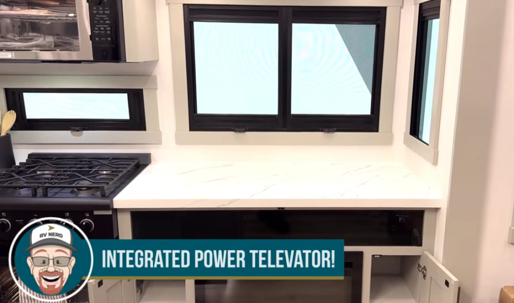 RV kitchen with large rear countertop, three panoramic windows, gas stove, and integrated power televator hidden beneath the counter.
