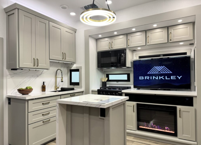 Luxury Brinkley RV kitchen with modern cabinetry, center island, LED lighting, large TV, gas range, and built-in electric fireplace.