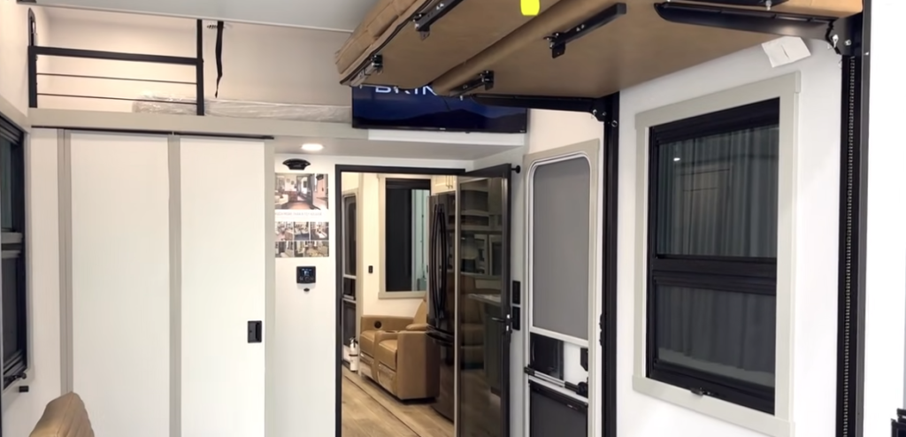 Brinkley toy hauler garage with overhead power-lift bunk, loft storage area, and sliding door entry leading into the main living space.