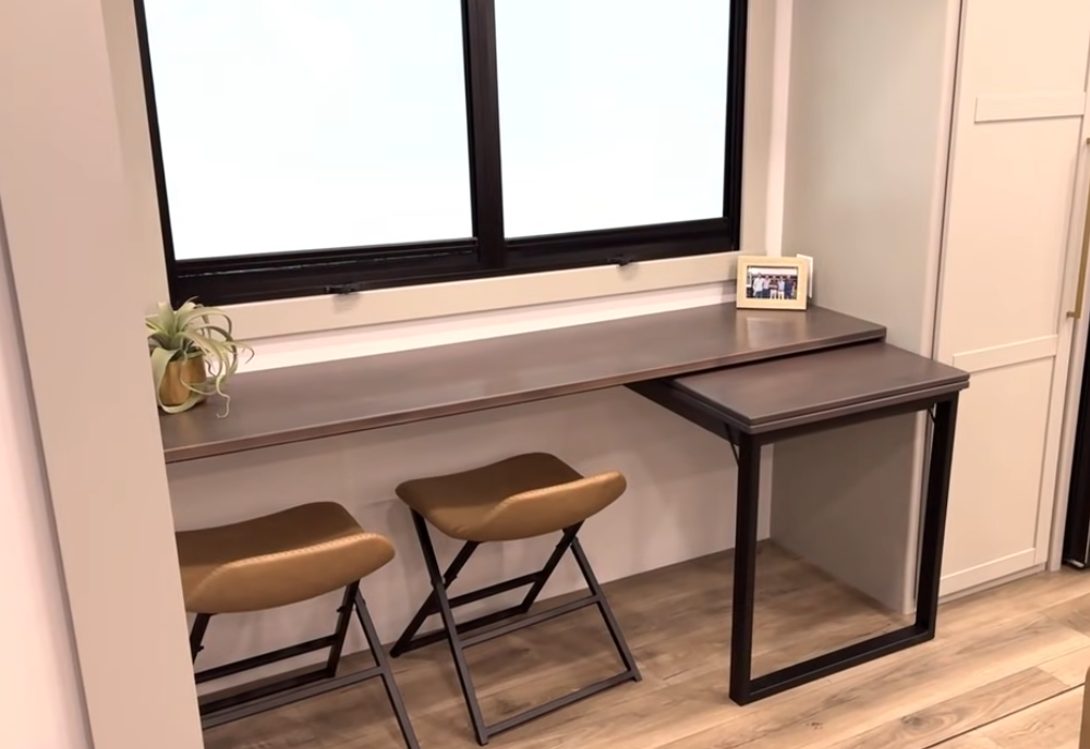 Convertible dining table and L-desk workspace in the Brinkley Model Z 3200 fifth wheel, featuring dual stools, large window, pull-out desk extension, and modern RV interior design