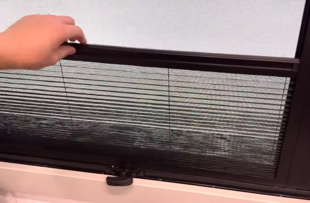 Hand adjusting the dual-pane RV window with integrated bug screen and privacy shade in the Brinkley Model Z 3200, showing easy light and airflow control