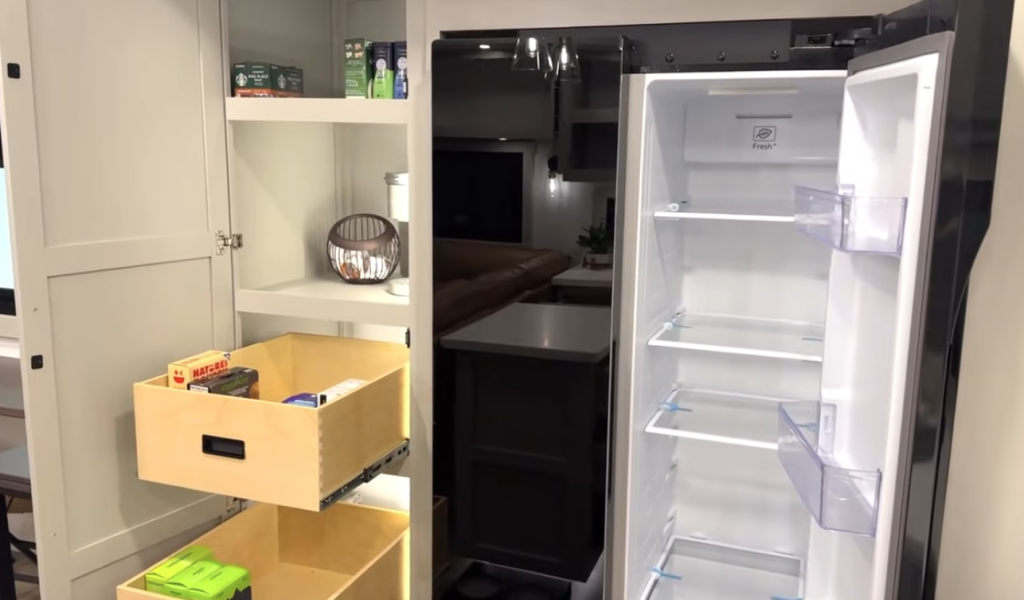Brinkley Model Z 3200 kitchen pantry with adjustable shelves and pull-out dovetail drawers beside a tall residential-style refrigerator, showcasing organized RV food storage space.