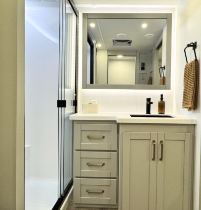 Brinkley Model Z 3200 bathroom vanity with solid-surface countertop, storage drawers, modern faucet, large framed mirror, and glass-door shower beside it.