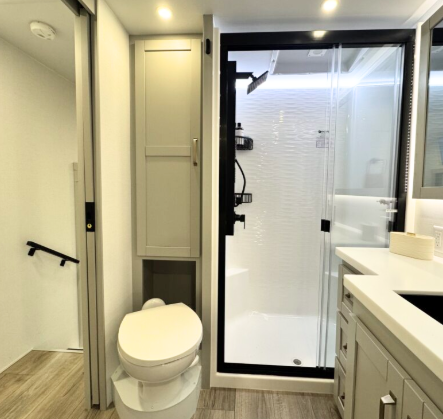 Brinkley Model Z 3200 RV bathroom with residential-style shower and glass doors, modern vanity with solid-surface countertop, storage cabinet, and foot-flush toilet.