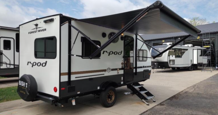 Forest River R-Pod travel trailer parked with awning extended, showcasing lightweight design, off-road tires, and compact camping setup