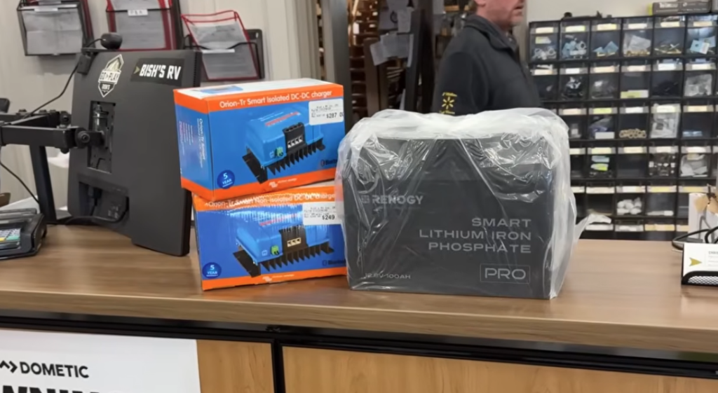 RV lithium battery upgrade components on a service counter, including a Renogy smart lithium iron phosphate battery and Orion DC-DC chargers at an RV service department.