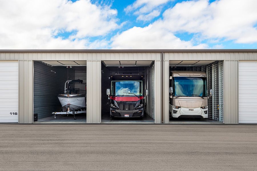 Enclosed indoor storage units housing a boat and two Class A motorhomes, demonstrating secure climate-protected RV and boat storage for off-season or winter parking.