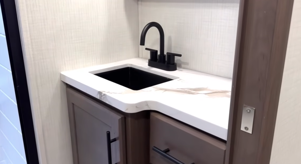 RV bathroom vanity with matte black faucet, integrated black sink, solid-surface countertop, and modern cabinetry, showcasing a compact, residential-style sink setup designed for durability and efficient RV bathroom use.