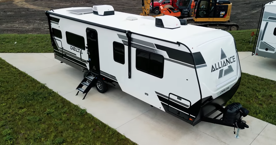 Alliance Delta travel trailer parked on a concrete pad, featuring modern exterior graphics, power awning, rooftop air conditioners, and compact single-axle design ideal for lightweight towing and family camping.