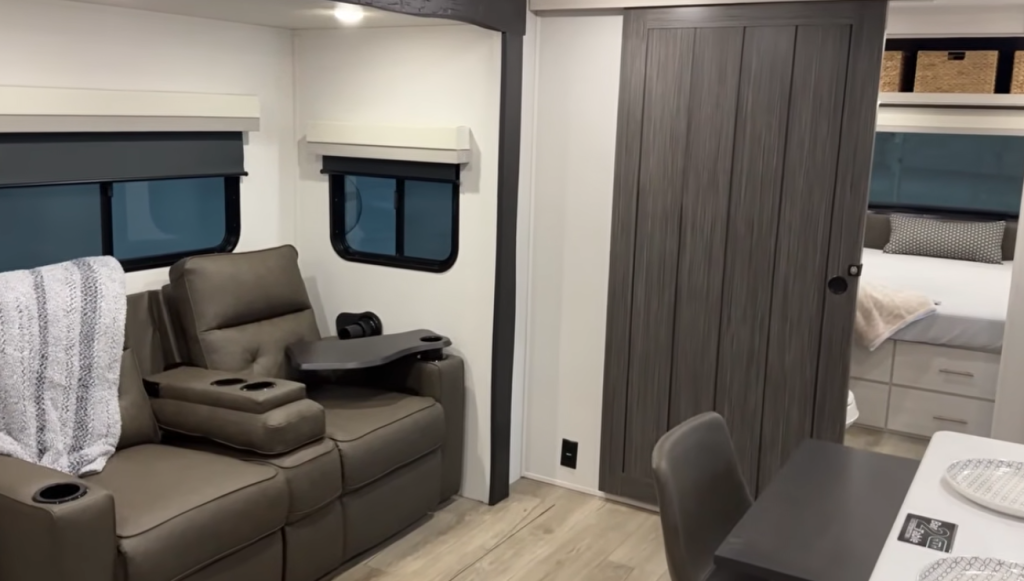 RV interior showing theater seating, sliding bedroom door, and view into the rear bedroom area
