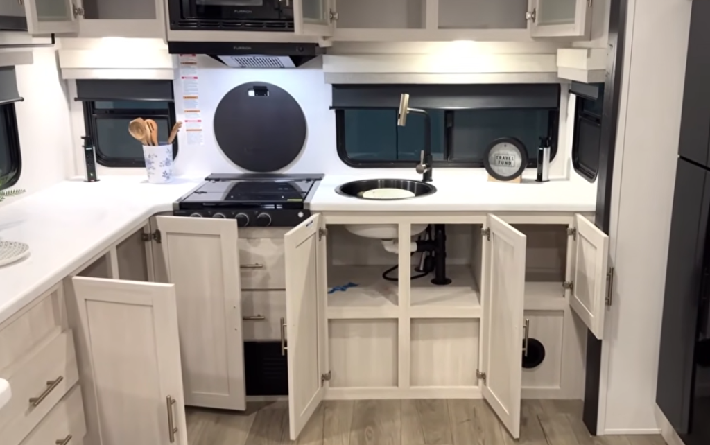 Travel trailer kitchen with cabinets open showing under-sink and drawer storage space