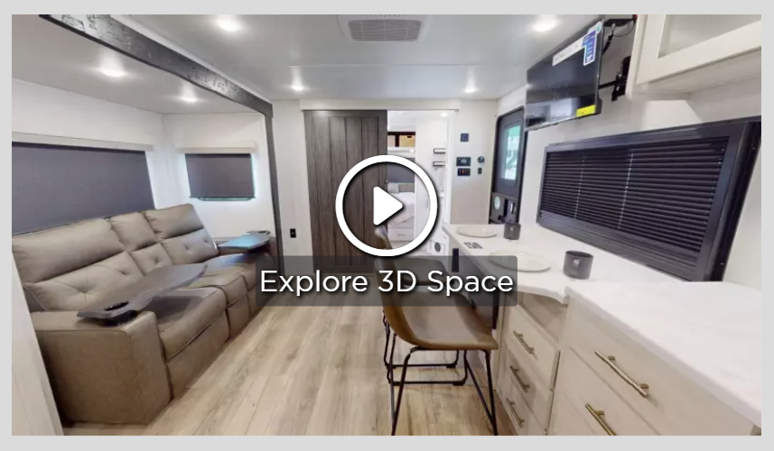 Travel trailer interior showing living area, sofa, kitchen counter, and dinette workspace