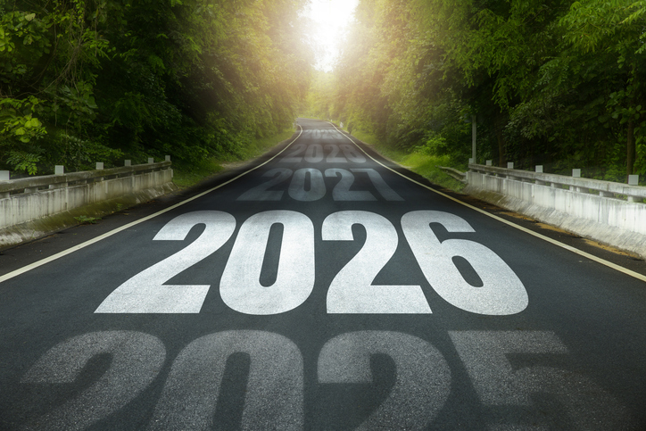 Long road through green forest with large 2026 painted on asphalt and earlier years fading ahead, 