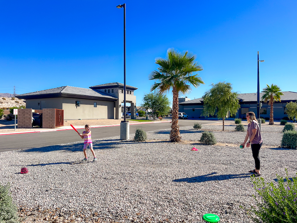 Family playing catch and games in open recreation area at a desert RV resort with palm trees and clear blue sky