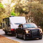 Pickup truck towing a travel trailer down a tree-lined road, with a passenger waving out the window.