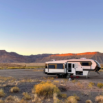 Fifth wheel RV parked in a desert landscape at sunset with mountains in the background and slide-out extended.