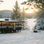 Snow-dusted Michigan campground at sunrise, one modern RV parked near pine trees, warm interior glow, subtle holiday lights along the awning, clean cinematic style, shallow depth of field, soft neutral palette.