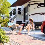 Young couple sits on chairs near camping trailer and car